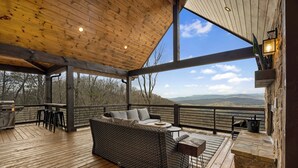A covered outdoor seating area with a wicker sofa, a table, and a grill.