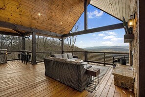A covered outdoor seating area with a wicker sofa, a table, and a grill.