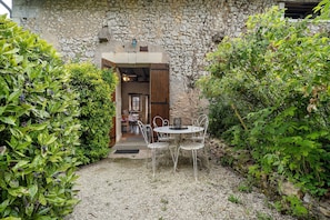 Un bâtiment en pierre avec un chemin de gravier menant à une table et des chaises en métal peintes en blanc.