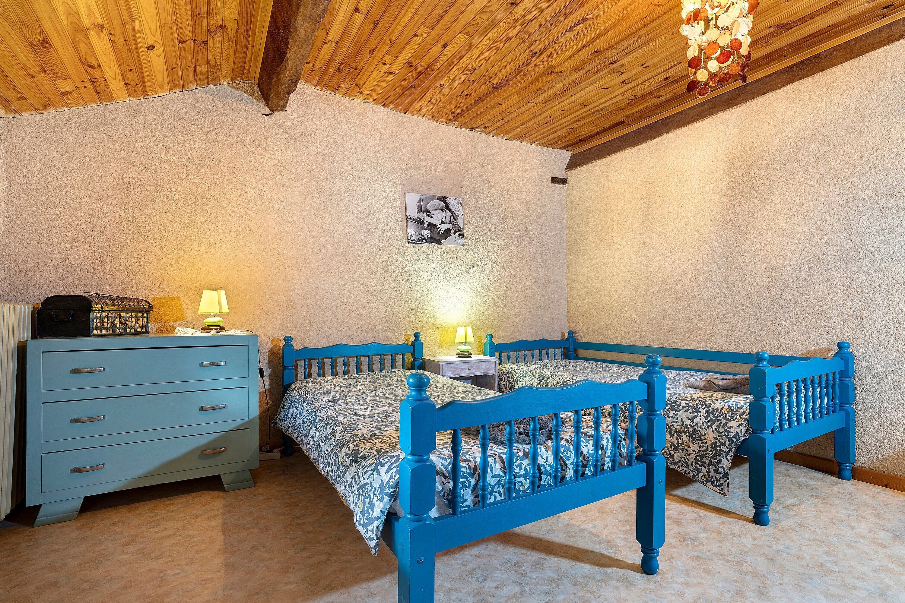 Une chambre avec deux lits, une commode et un luminaire au plafond.