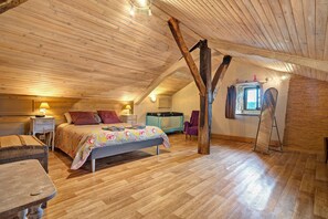 A bedroom with a wooden ceiling, a bed with floral bedding, a nightstand, a dresser, and a window with a view.