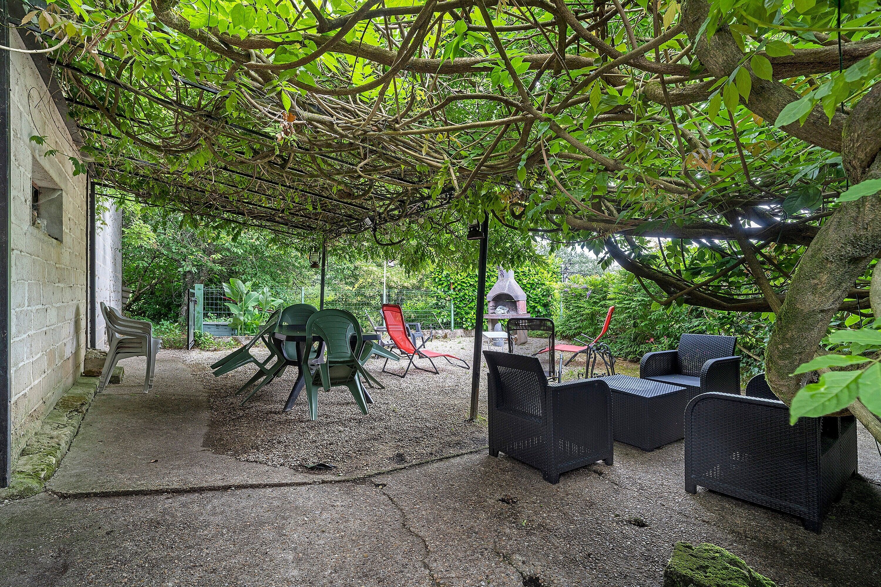 Un espace extérieur aménagé, abrité et doté de chaises et d’une table, entouré d’arbres et de verdure.
