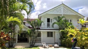Une maison à deux étages avec une piscine, entourée de plantes tropicales et agrémentée d’un cygne flottant.