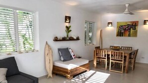 Un salon comprenant un canapé, un banc en bois, une table à manger avec des chaises et une planche de surf.