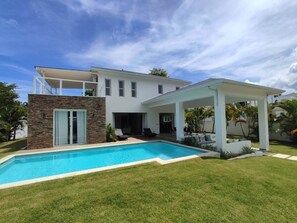Ett modernt hus med en swimmingpool, en täckt uteplats och en fasad av sten.