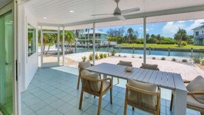 A covered outdoor area with a table and chairs, a ceiling fan, and a view of a pool and greenery. - Experience waterfront vacation  living (Englewood)