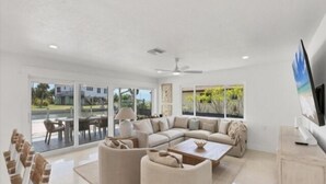 A spacious living room with a large sectional sofa, a coffee table, and a TV. There are large windows offering a view of the outdoors. - Experience waterfront vacation  living (Englewood)