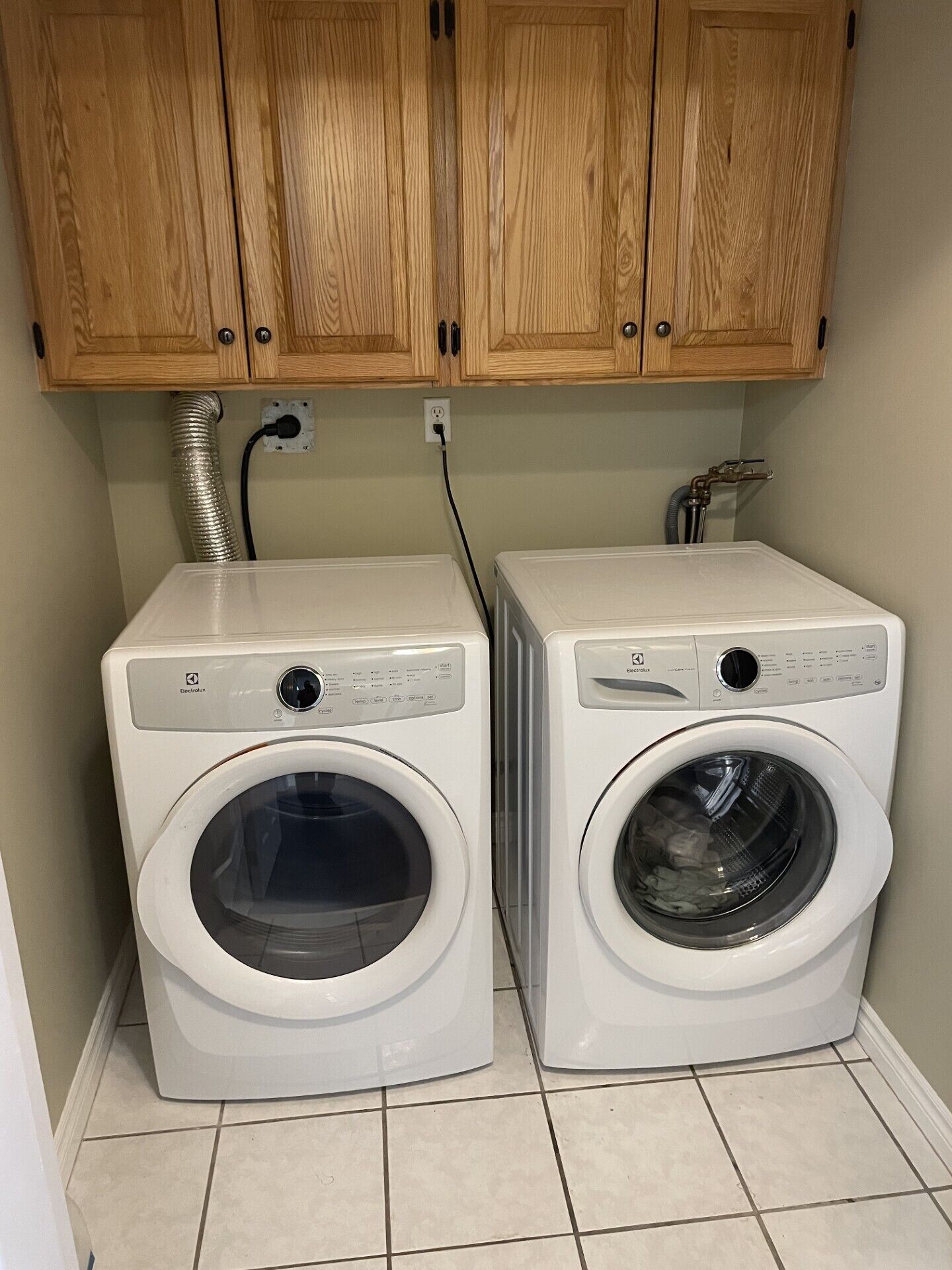 Two white front-loading washing machines in a laundry room with wooden cabinets above.