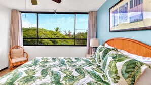 A bedroom with a bed, a ceiling fan, a window with a view of greenery, and a framed picture on the wall. - Sea Turtle Suite - Steps from Carlsmith Beach! (Hilo)
