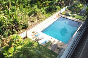 An outdoor swimming pool with lounge chairs and a small table, surrounded by lush greenery. - Sea Turtle Suite - Steps from Carlsmith Beach! (Hilo)