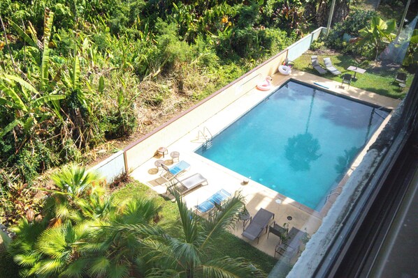 An outdoor swimming pool with lounge chairs and a small table, surrounded by lush greenery.