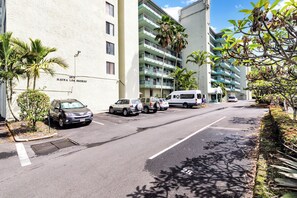 A parking lot with several cars, a building with balconies, and palm trees. - Sea Turtle Suite - Steps from Carlsmith Beach! (Hilo)