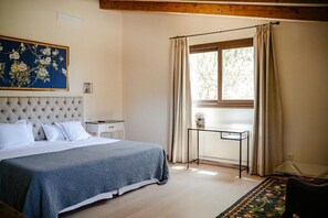 A bedroom with a large bed, a window with curtains, a small table, and a painting on the wall. - Charming 7-bedroom villa in the heart of the Balearic Islands, Majorca! (llucmajor)