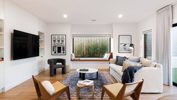A modern living room with a flat-screen TV, a sofa, two wooden chairs, a coffee table, and a large window with a view of greenery. - 1 Beach House - Award-winning Luxury Smart Home (Warrnambool)
