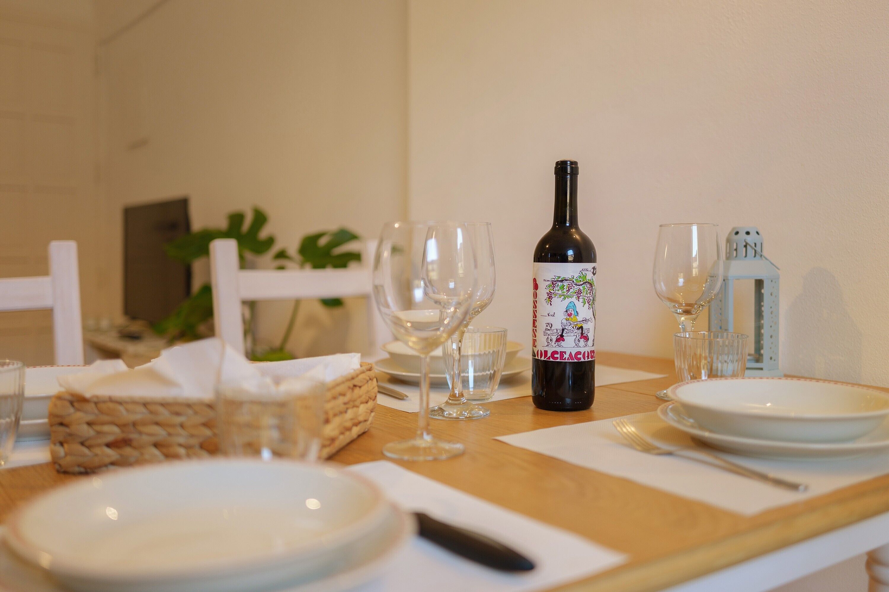 Une table à manger avec des assiettes, des verres, une bouteille de vin et un panier de viennoiseries.