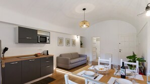 Una cucina moderna con forno a microonde integrato, una zona pranzo con tavolo apparecchiato per due e un divano sullo sfondo.