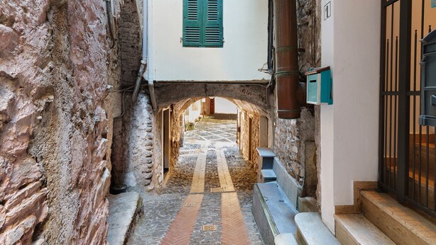 Un stretto vicolo con pareti in pietra, una porta in legno e un pavimento piastrellato.