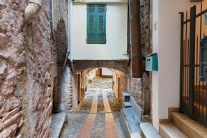 Une ruelle étroite aux murs de pierre, avec une porte en bois et un sol carrelé.