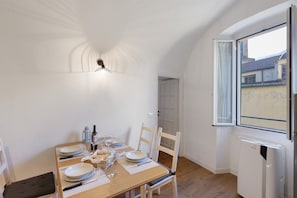 Zona pranzo con tavolo imbandito per quattro persone, sedie, lampada a soffitto e finestra vista edifici.