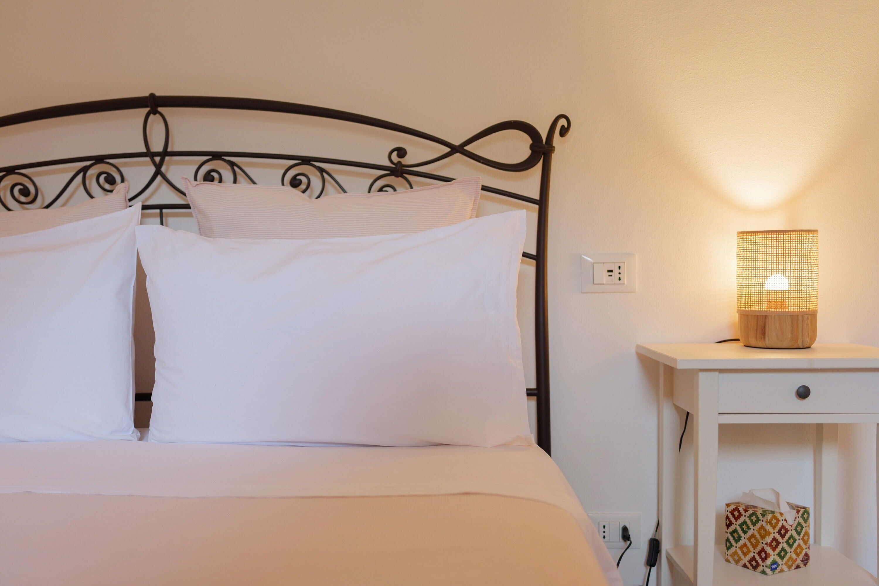 Un lit avec une literie blanche, une table de chevet avec une lampe et une prise électrique au mur.