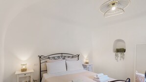 Un letto rifatto con lenzuola bianche, un comodino con una lampada e una pianta pensile.