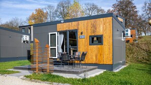 A modern, compact building with a wooden exterior, a patio with outdoor seating, and a clear sky.