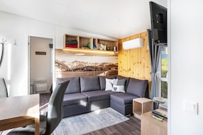 Un salon moderne avec un canapé d’angle, une table à manger et un téléviseur fixé au mur.