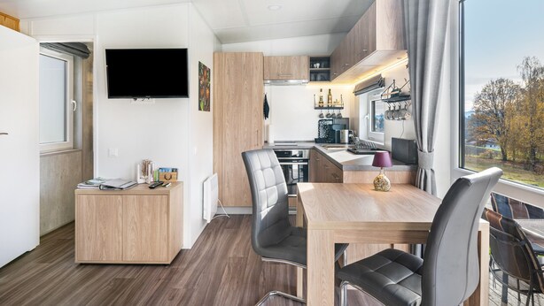 A modern kitchen with a dining area, a flat-screen TV, and a view of the outdoors.