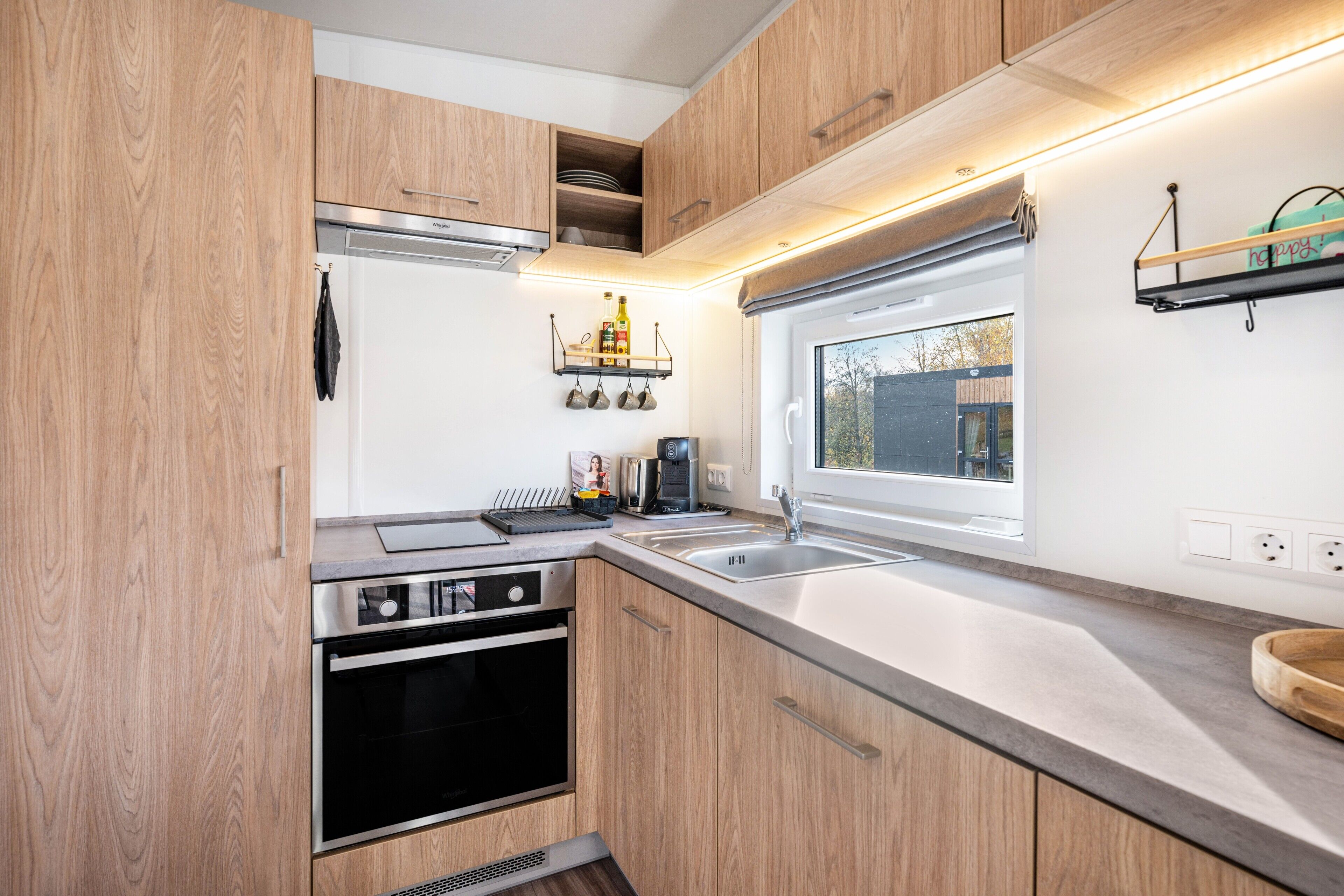 A compact kitchen with wooden cabinets, a built-in oven, a sink, and a window.