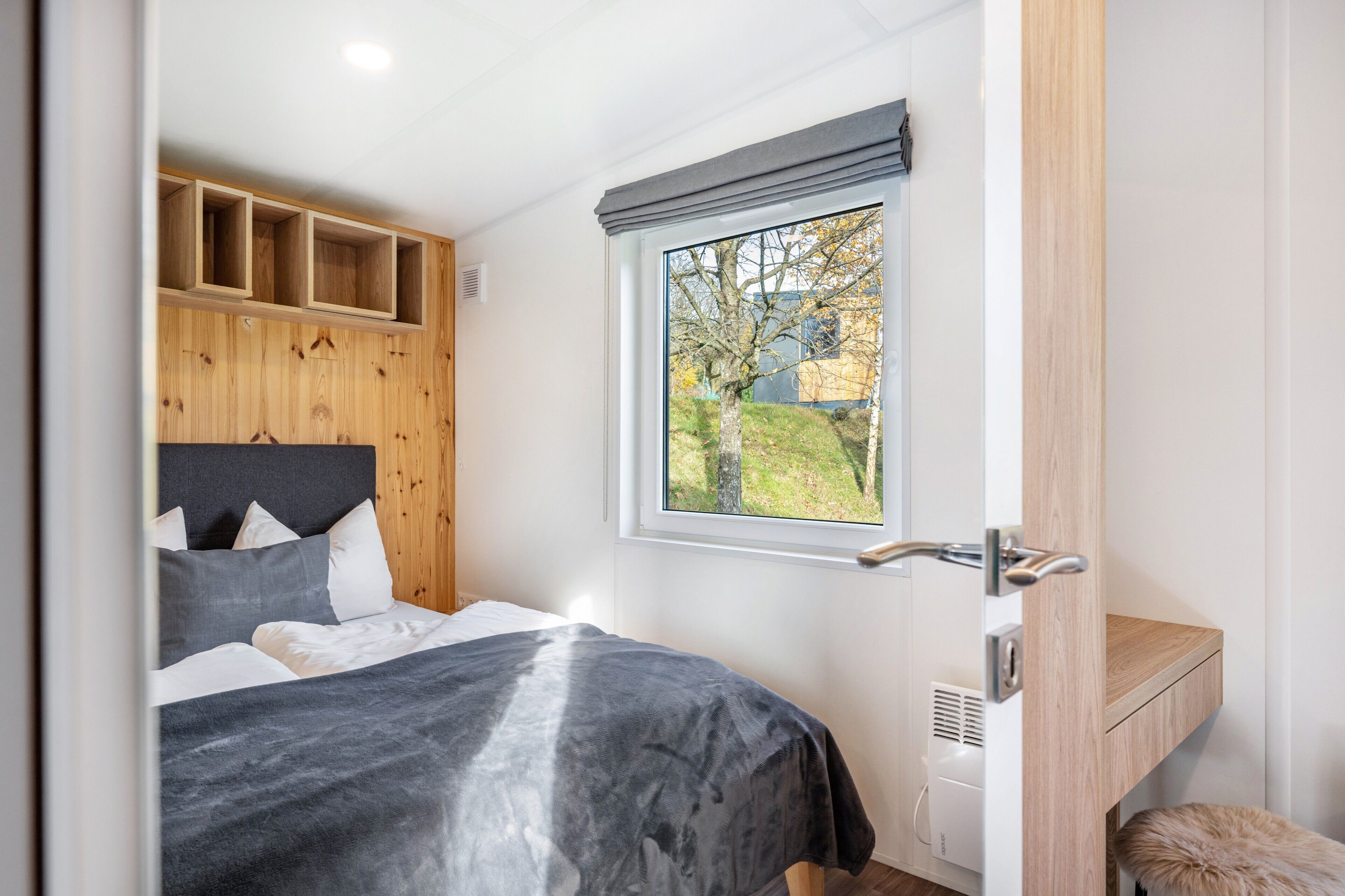 Une chambre à coucher avec un lit, une fenêtre donnant sur un beau paysage, une tête de lit en bois et une étagère intégrée.