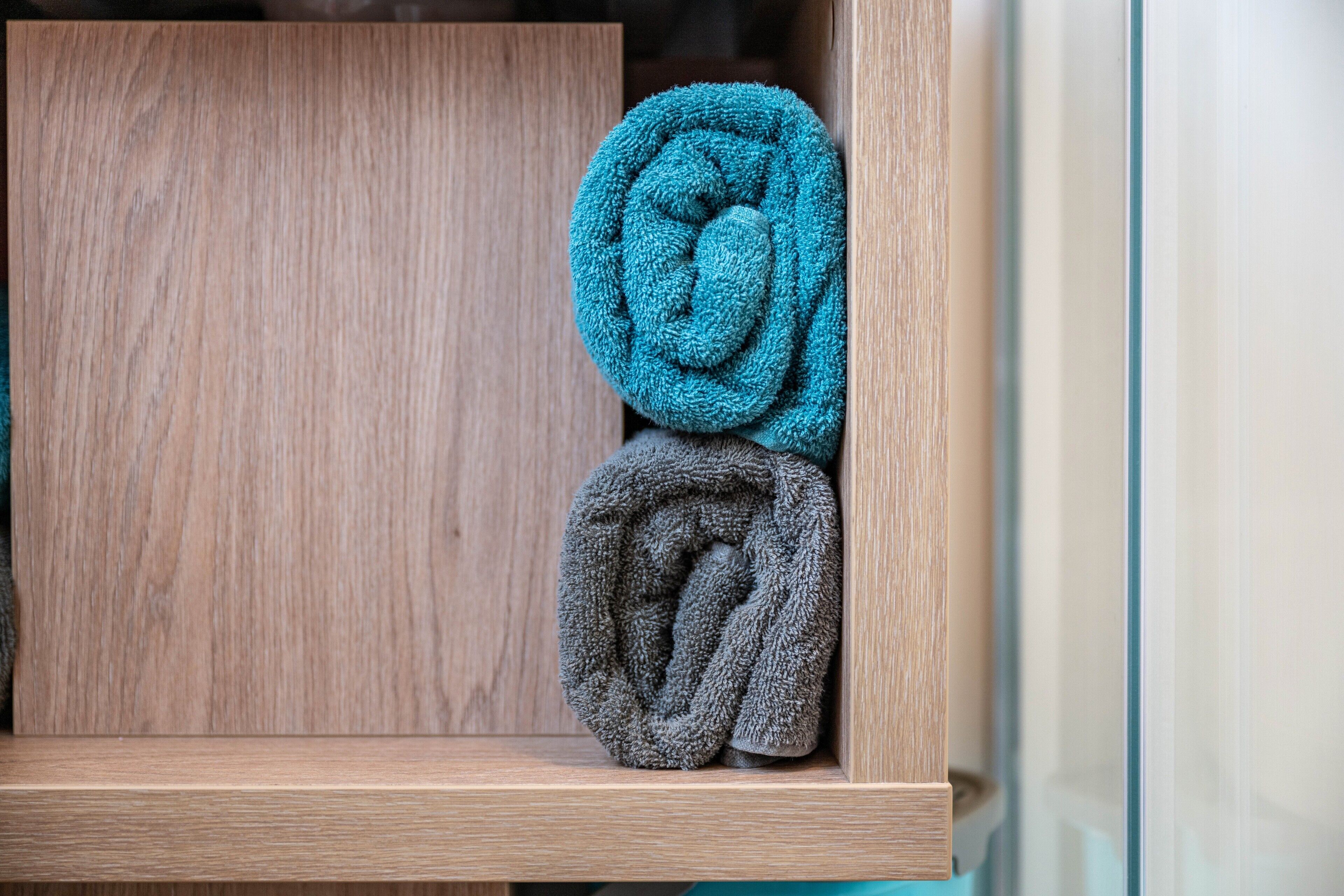 Ein Holzregal mit zwei aufgerollten Handtüchern, eines türkis und eines grau.
