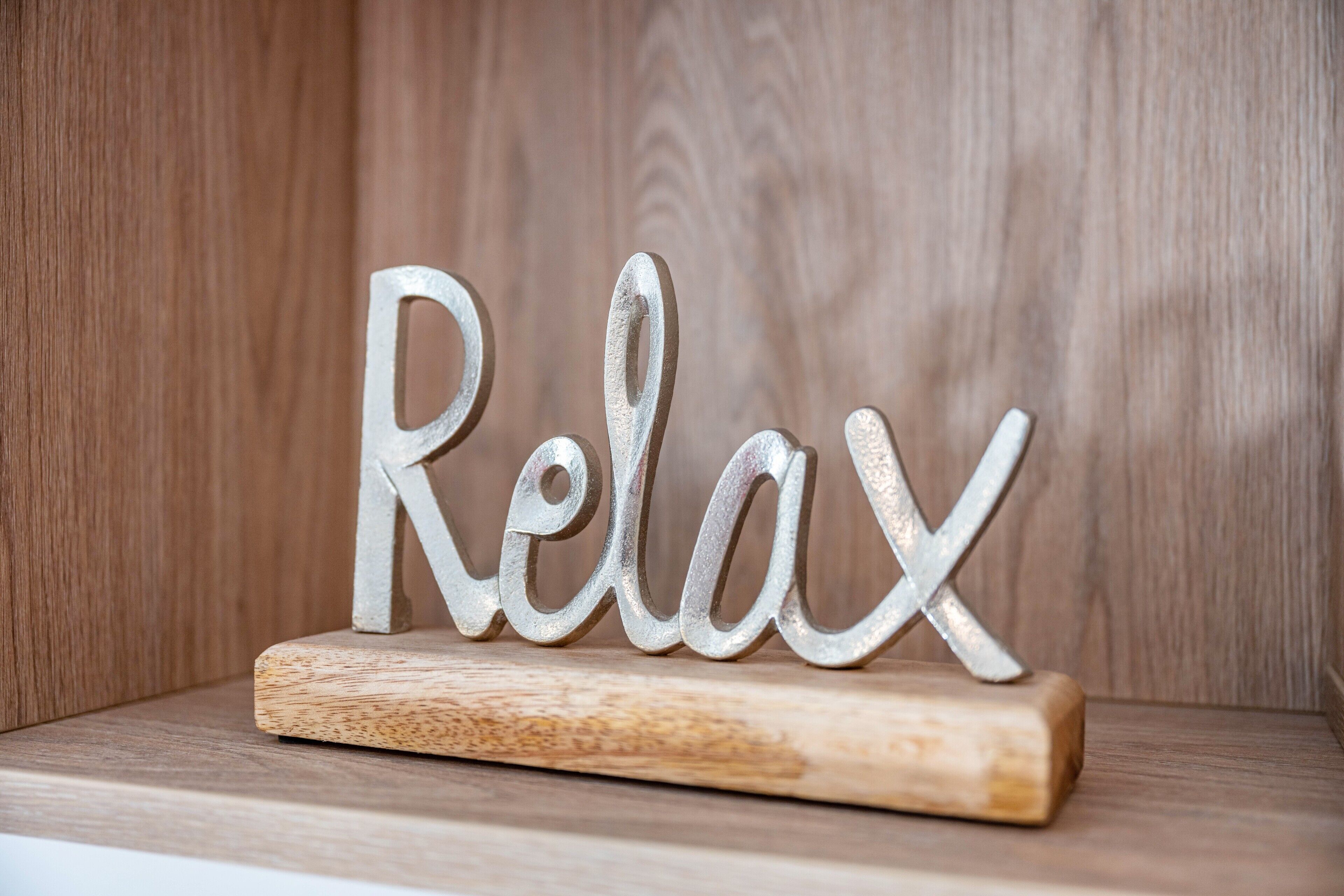 A wooden shelf with a metal sign spelling 'Relax' on it.