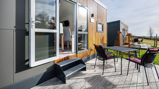 Un bâtiment moderne doté d’une terrasse, de sièges extérieurs et d’une grande porte-fenêtre coulissante.