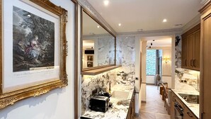 Cozinha moderna com bancadas de mármore, uma pia e uma torradeira. Há uma obra de arte emoldurada na parede e um espelho acima da pia.