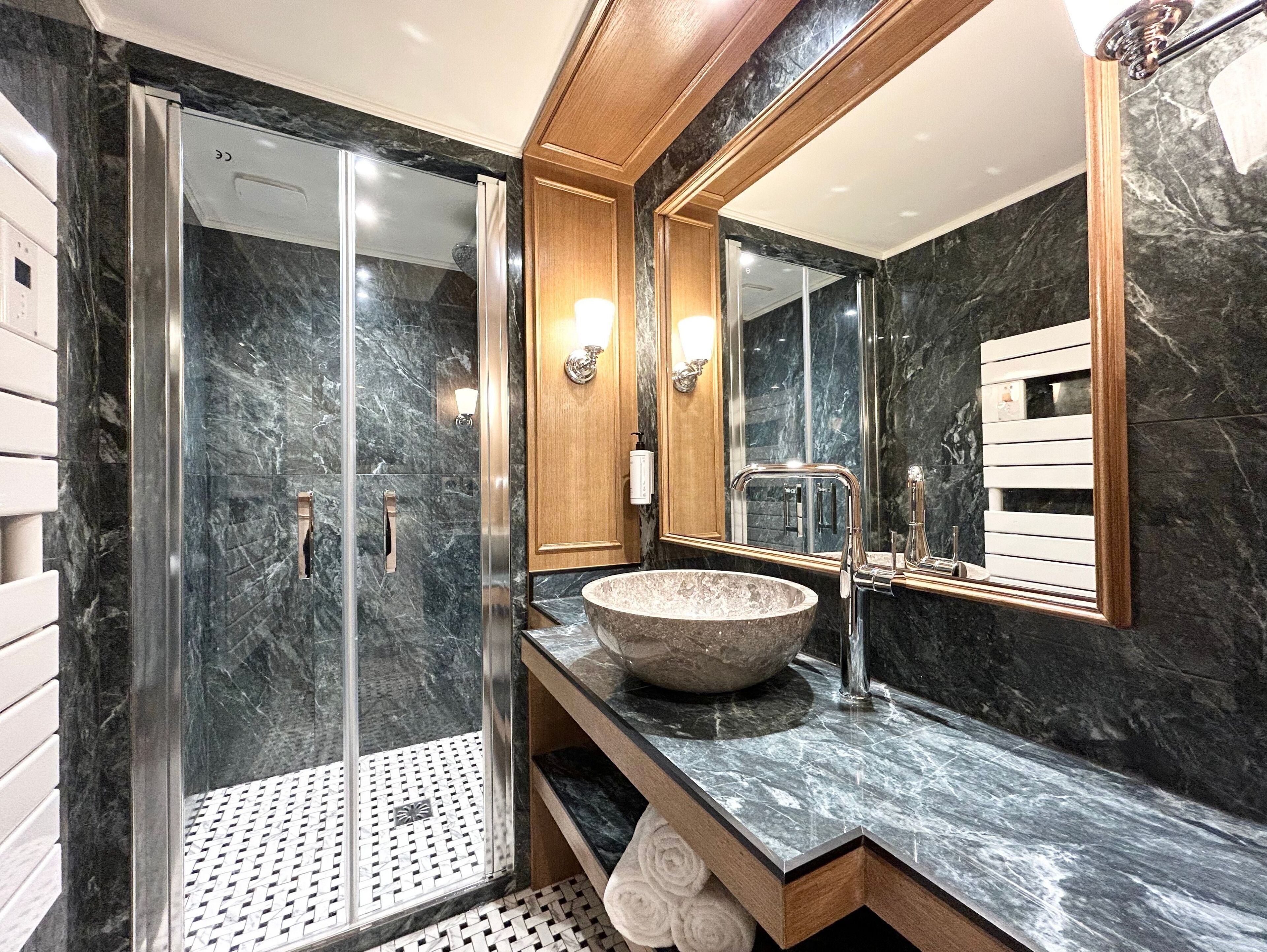 Un baño moderno con ducha envuelta en vidrio, un espejo grande y una encimera de mármol.