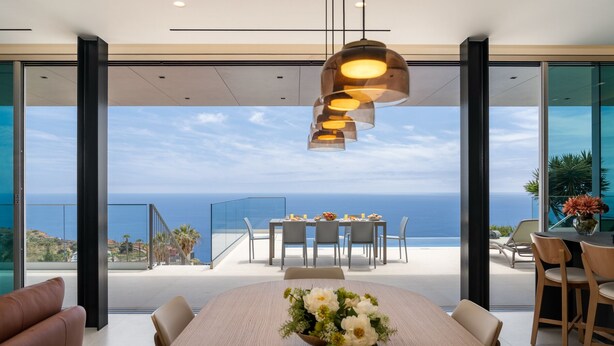 A dining area with a view of the ocean, featuring a large table, chairs, and a hanging light fixture. - Superb Top Luxury Villa|GrandView Cristo Rei (Canico)