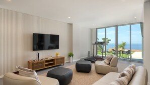 A modern living room with a flat-screen TV, comfortable seating, and a balcony with a view of the ocean. - Superb Top Luxury Villa|GrandView Cristo Rei (Canico)