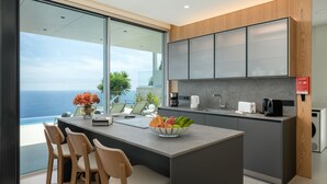 A modern kitchen with a large island, a dining area with chairs, and a view of the ocean. - Superb Top Luxury Villa|GrandView Cristo Rei (Canico)