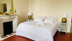A neatly made bed with white linens, two bedside tables with lamps, a white fireplace, and a tiled floor. - House on large 200-hectare estate with swimming pool (Esparron)