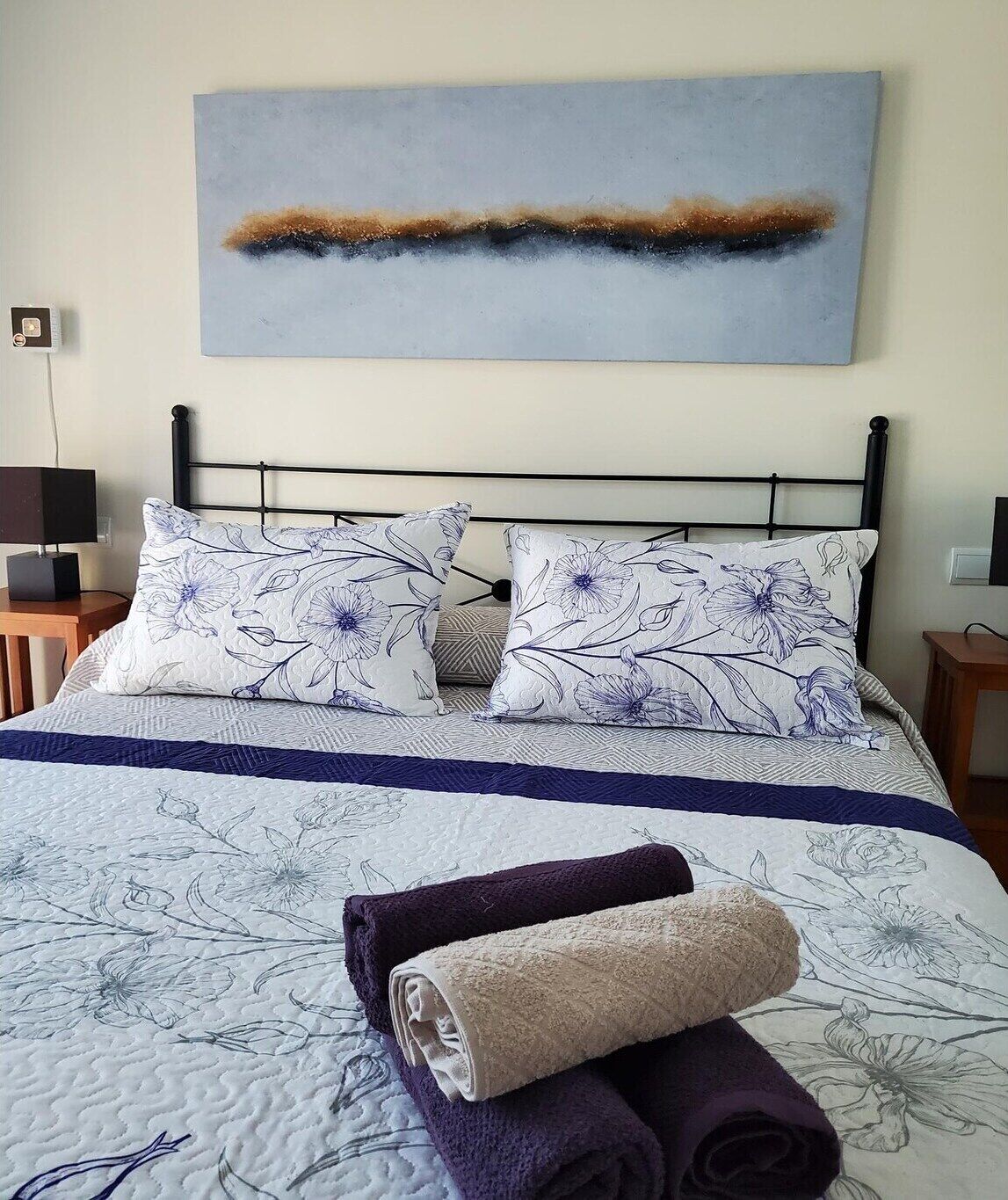Cama bem arrumada com almofadas estampadas e colcha azul e branca.