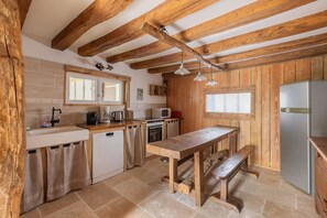 A rustic kitchen with wooden beams, a wooden table, a bench, a refrigerator, and a window. - Family Cottage Near Beauval Zoo (NOUANS LES FONTAINES)