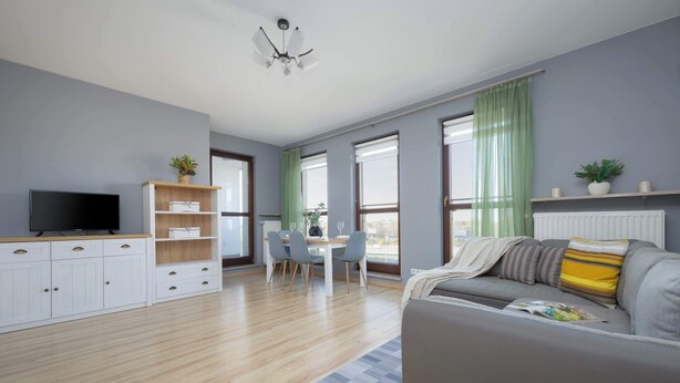 Ein modernes Wohnzimmer mit grauem Sofa, Holzboden, Fernseher, Essbereich mit Stühlen und großen Fenstern mit grünen Vorhängen.