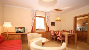 A room with a bed, a desk with a computer, a dining table with chairs, a kitchen area, and a ceiling fan. - Apartment '12' with Mountain View, Shared Garden and Wi-Fi (Schladming)