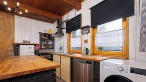 A kitchen with a wooden countertop, a dishwasher, a washing machine, and a window with curtains. - Spacious Apartment in Szczyrk | Garden | Parking (Szczyrk)