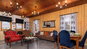 A cozy living room with wooden paneling, a red armchair, a brown sofa, and a dining table with blue chairs. - Spacious Apartment in Szczyrk | Garden | Parking (Szczyrk)