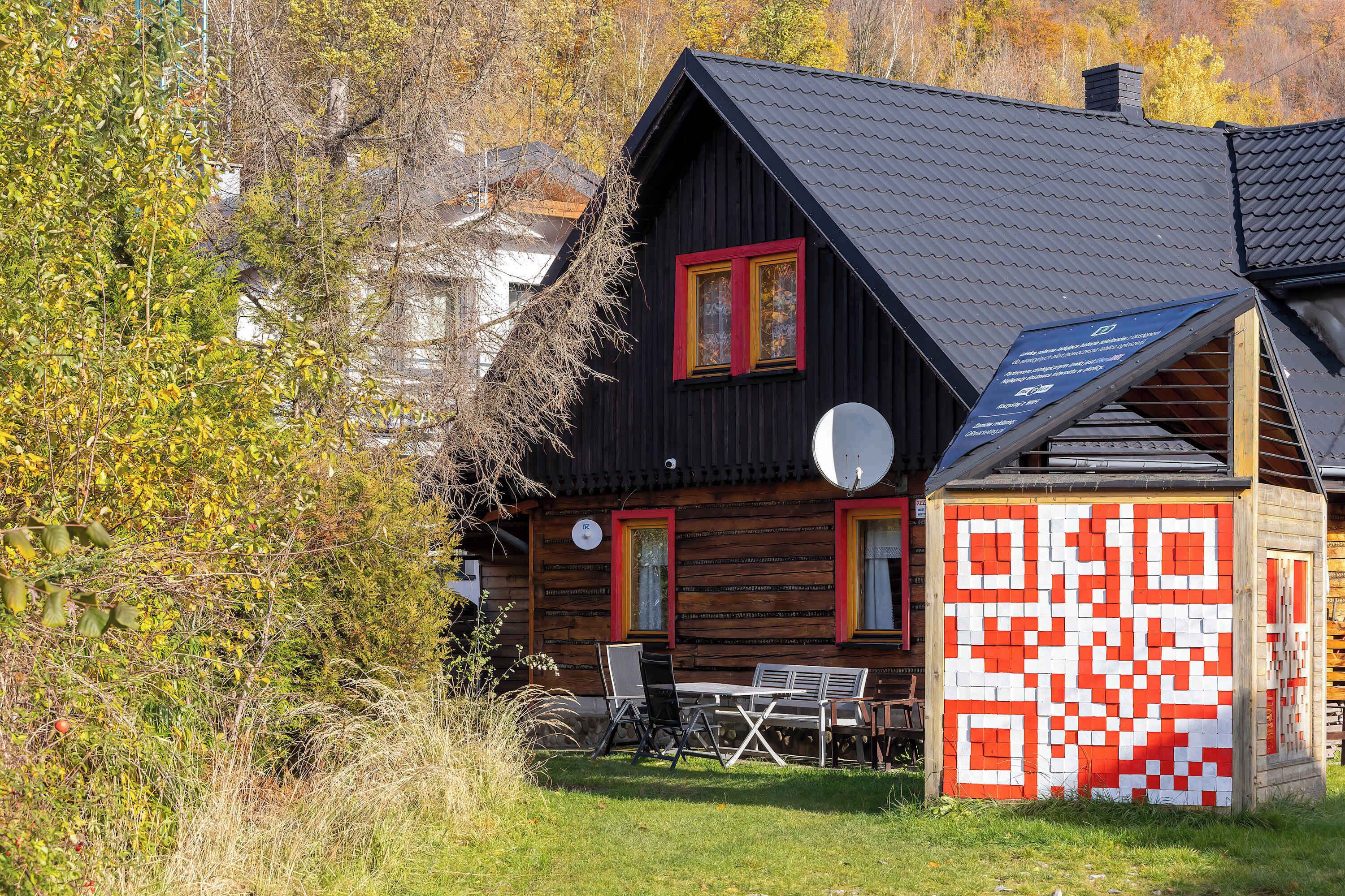A wooden house with a black roof, red-framed windows, and a QR code mural.