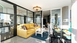 Uma sala de estar moderna com um sofá amarelo, uma mesa de centro branca e uma área de jantar com mesa e cadeiras de vidro.