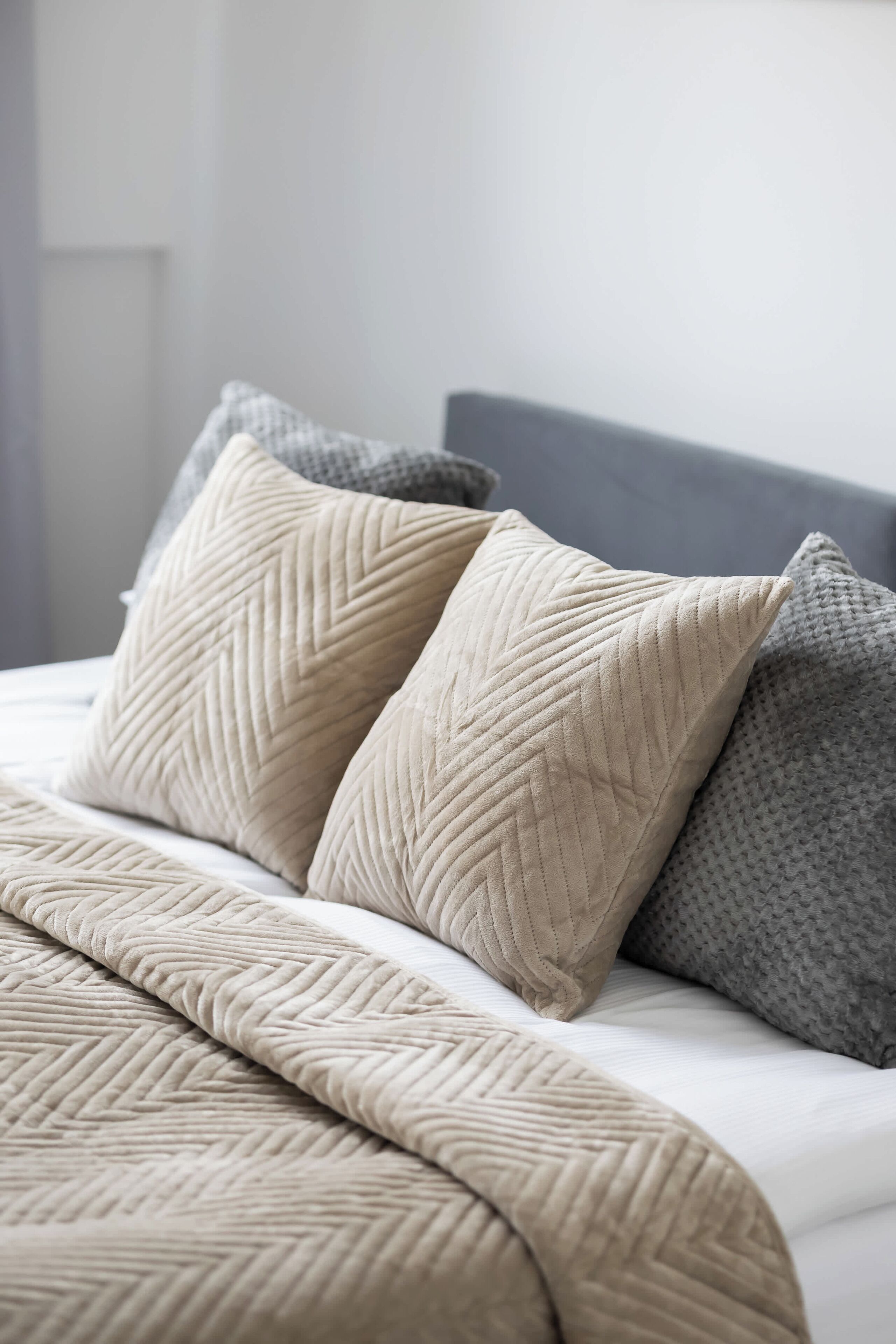 A bed with beige and gray pillows and a textured beige blanket.