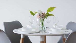 A round dining table with four grey chairs, a white vase with flowers, and clear glassware. - Spacious Apartment | 3 Bedrooms, Balcony, Close to Metro (Warszawa)