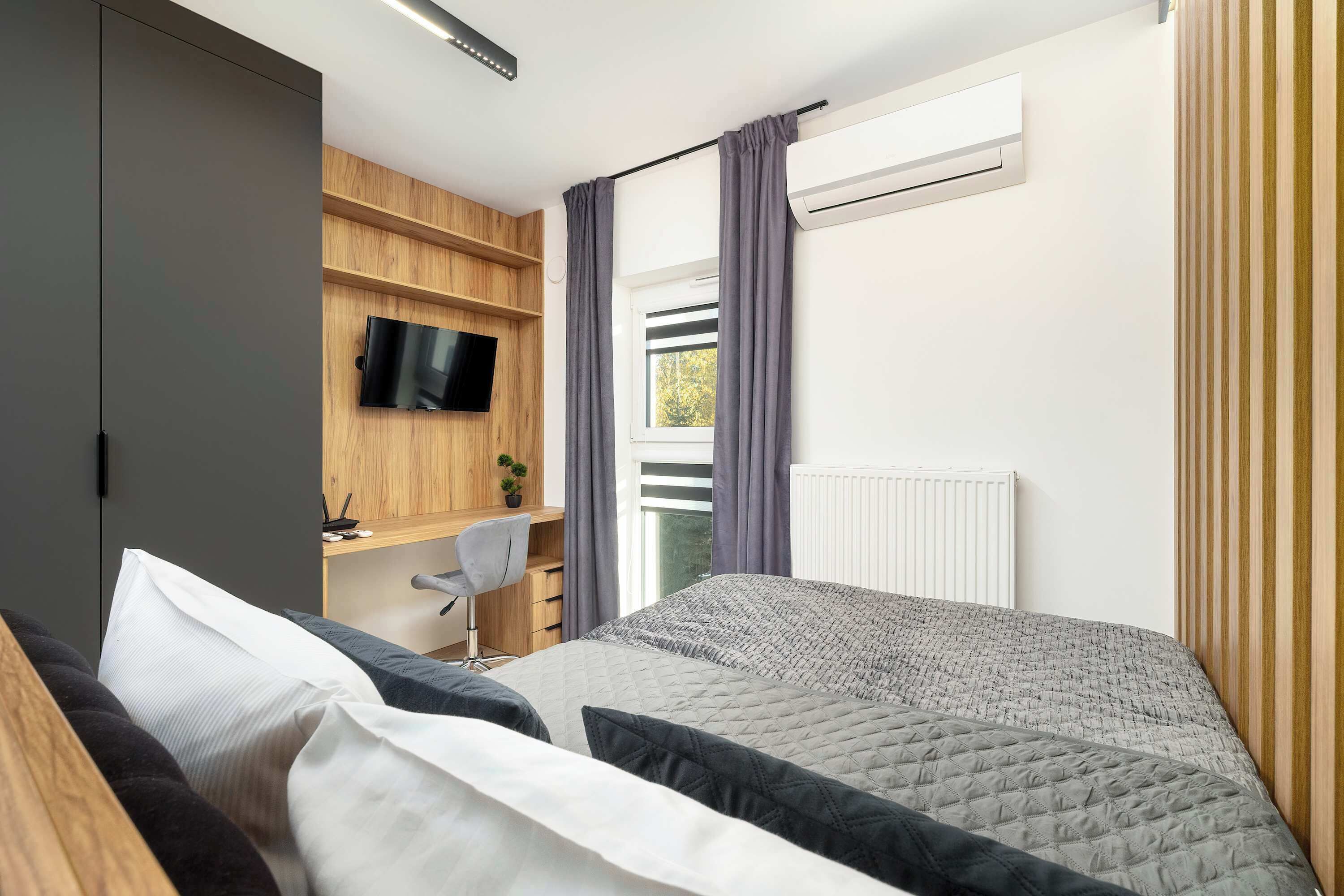 Une chambre à coucher moderne avec un lit, un bureau et un téléviseur fixé au mur.